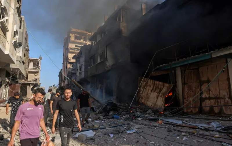 Palestinians walk amid the rubble of a building hit in an Israeli air strike on October 13, 2023. Israel has called for the immediate relocation of 1.1 million people in Gaza amid its massive bombardment in retaliation for Hamas's attacks, with the United Nations warning of "devastating" consequences. (Photo by MOHAMMED ABED / AFP)