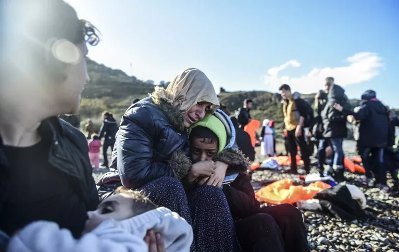 Women and children react as they sit on shore after arriving with other migrants and refugees on the Greek island of Lesbos by crossing the Aegean Sea from Turkey on November 26, 2015. More than 800,000 migrants and refugees have crossed the Mediterranean to Europe this year, the UN said on November 13, warning the Greek island of Lesbos especially was overstretched, with thousands, including young children, forced to sleep outside. / AFP / BULENT KILIC