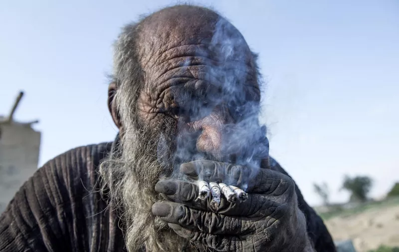 Amou Haji (uncle Haji) smokes several cigarettes as he sits on the ground on the outskirts of the village of Dezhgah in the Dehram district of the southwestern Iranian Fars province, on December 28, 2018. - Believed to be the worlds dirtiest man, villagers say that Haji's leather-like skin hasn't touched soap and water for more than sixty years. They believe that he decided to live in isolation after suffering from an emotional setback in his youth. (Photo by AFP)
