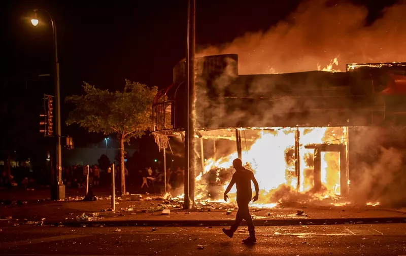 A man walks past a liquor store in flames near the Third Police Precinct on May 28, 2020 in Minneapolis, Minnesota, during a protest over the death of George Floyd, an unarmed black man, who died after a police officer kneeled on his neck for several minutes. - A police precinct in Minnesota went up in flames late on May 28 in a third day of demonstrations as the so-called Twin Cities of Minneapolis and St. Paul seethed over the shocking police killing of a handcuffed black man. The precinct, which police had abandoned, burned after a group of protesters pushed through barriers around the building, breaking windows and chanting slogans. A much larger crowd demonstrated as the building went up in flames. (Photo by Kerem Yucel / AFP)