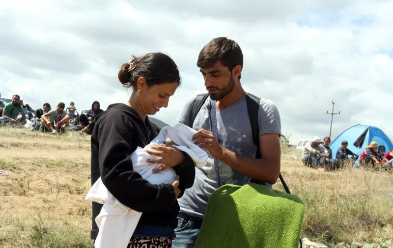 A Syrian migrant couple Syria carry their child in a temporary center for refugees on the border between Serbia and Macedonia near the village of Miratovac, in the municipality of Presevo, on August 23, 2015. The temporary center for migrants in the village Miratovac was formed on August 22 after a large influx of migrants from Macedonia. About 5,000 migrants are currently in the center waiting to be transported to a permanent center for migrants located in the town of Presevo. AFP PHOTO / SASA DJORDJEVIC