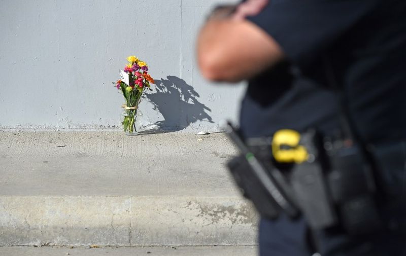 A San Bernardino police officer stands by a flowers on the sidewalk on Waterman Avenue near the Inland Regional Center on December 3, 2015 in San Bernardino, California. Police continue to investigate a mass shooting at the Inland Regional Center in San Bernardino that left at least 14 people dead and another 17 injured.  AFP PHOTO /ROBYN BECK / AFP / ROBYN BECK