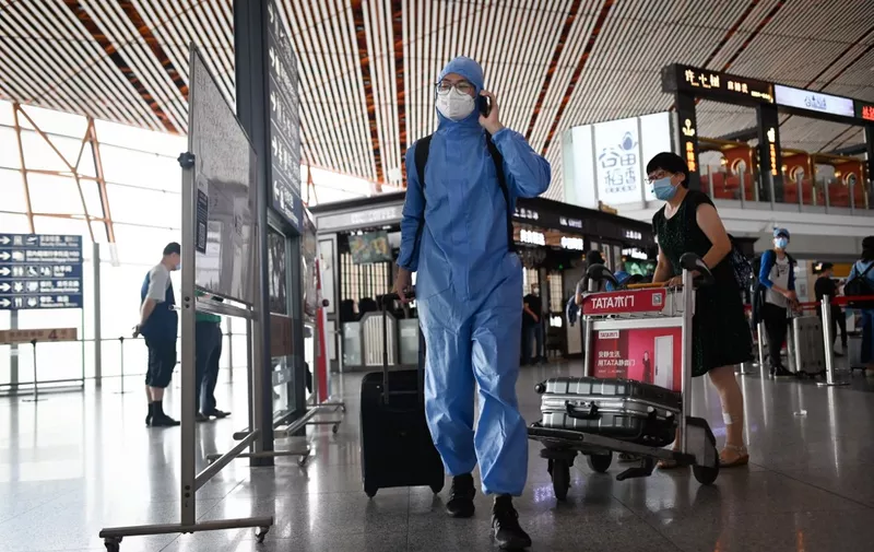 A man wearing a protective suit uses his phone at Beijing's international airport on June 17, 2020. - Beijing's airports cancelled more than 1,200 flights and schools in the Chinese capital were closed again on June 17 as authorities rushed to contain a new coronavirus outbreak linked to a wholesale food market. (Photo by STR / AFP)