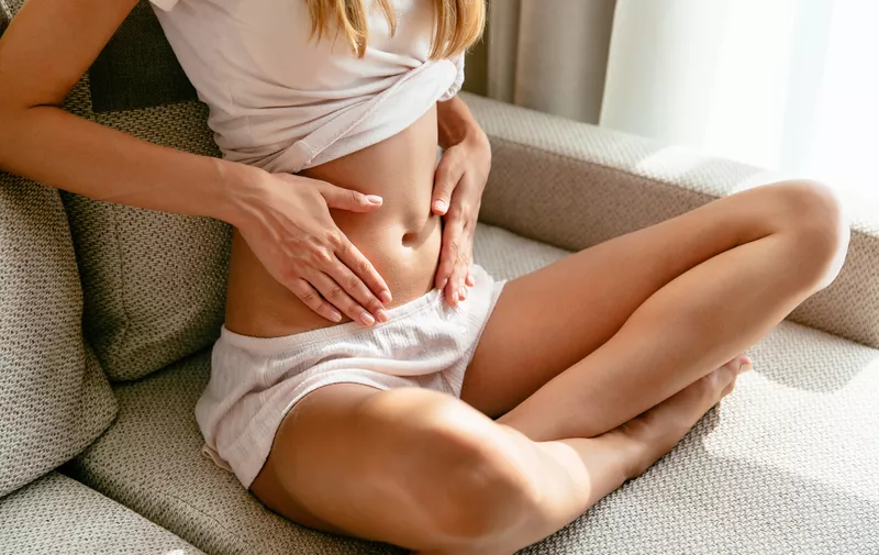 Pregnant Woman at an early pregnancy holding hands on belly sitting on sofa at home