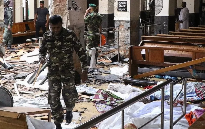 EDITORS NOTE: Graphic content / Sri Lankan security personnel walk past dead bodies covered with blankets amid blast debris at St. Anthony's Shrine following an explosion in the church in Kochchikade in Colombo on April 21, 2019. - A string of blasts ripped through high-end hotels and churches holding Easter services in Sri Lanka on April 21, killing at least 156 people, including 35 foreigners. (Photo by ISHARA S.  KODIKARA / AFP)