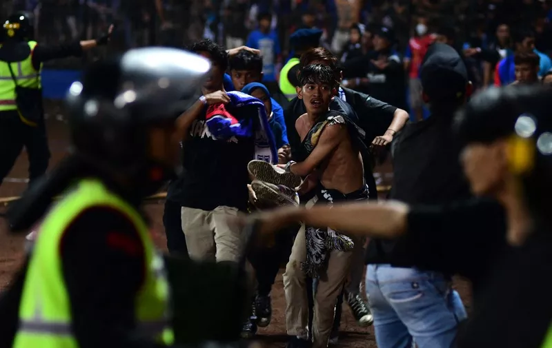 In this picture taken on October 1, 2022, a group of people carry a man after a football match between Arema FC and Persebaya Surabaya at Kanjuruhan stadium in Malang, East Java. - At least 127 people died at a football stadium in Indonesia late on October 1 when fans invaded the pitch and police responded with tear gas, triggering a stampede, officials said. (Photo by AFP)