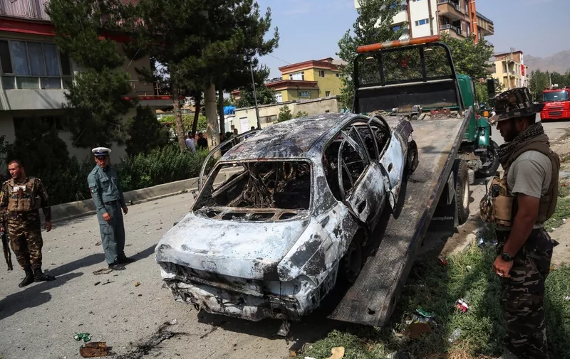 Afghan security personnel stand guard near a charred vehicle from which rockets were fired that landed near the Afghan presidential palace in Kabul on July 20, 2021. (Photo by - / AFP)