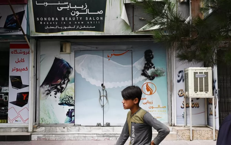 A youth walks past a closed beauty salon with images of women defaced at Shahr-e Naw area in Kabul on July 4, 2023. Afghanistan's Taliban authorities have ordered beauty parlours across the country to shut within a month, the vice ministry confirmed on July 4, the latest curb to further squeeze women out of public life. (Photo by Wakil Kohsar / AFP)