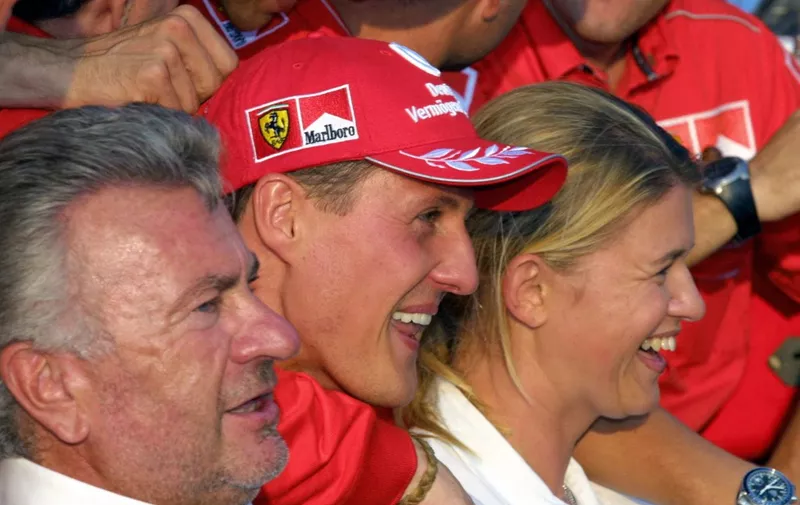 German Ferrari 2001 World Champion Michael Schumacher (C) sits between his wife Corinna and his manager Willi Weber (L) of Germany and all the Ferrari team celebrating their World Formula One titles obtained on the Hungaroring racetrack near Budapest, 19 August 2001.    AFP PHOTO PIERRE VERDY (Photo by PIERRE VERDY / AFP)