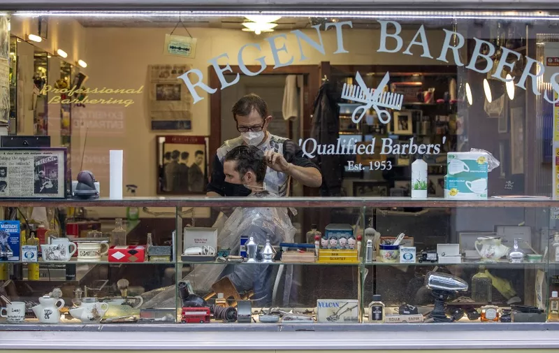 A barber wearing PPE of a face mask or covering due to COVID-19, cuts a customer's hair inside a Barbers in Dublin on October 19, 2020, amid reports that further lockdown restrictions could be imposed to help mitigate the spread of the novel coronavirus. - Ireland will crank up coronavirus restrictions, prime minister Micheal Martin said last week, announcing a raft of new curbs along the border with the British province of Northern Ireland. (Photo by PAUL FAITH / AFP)
