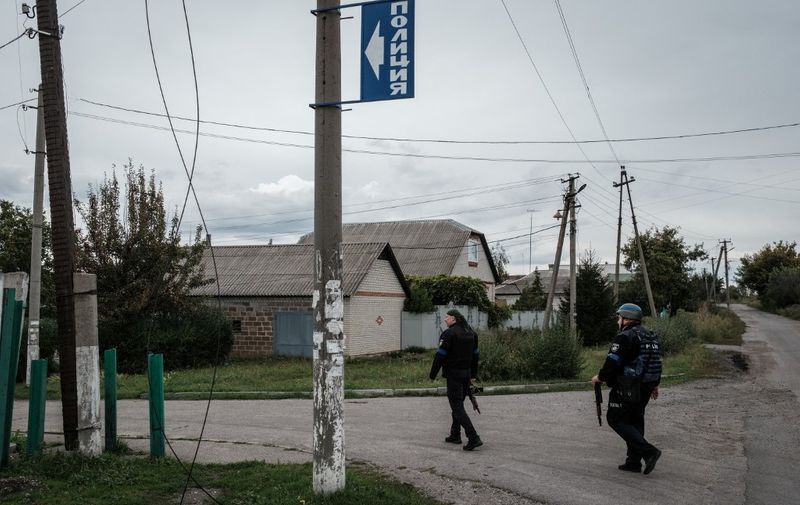 A blue sign reading "police" in Russian spelling is seen as police officers walk towards a police station used during the Russian occupation as a base by a local pro-Russian militia, in the retaken town of Kozacha Lopan, Kharkiv region, on September 20, 2022. - This month's dramatic Ukrainian advance north of Kharkiv drove Russian forces back across the border, and uncovered evidence of torture under their occupation. (Photo by Yasuyoshi CHIBA / AFP)