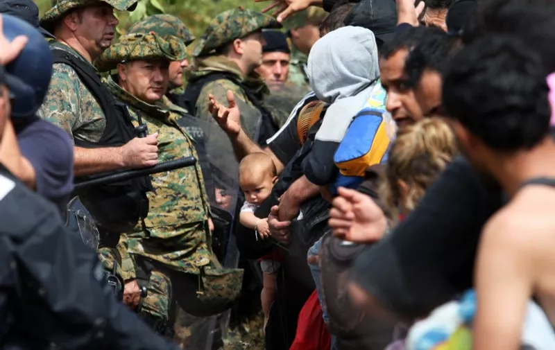 Migrants try to pass through Macedonian border police near to the town of Idomeni, on the Greece-Macedonia border on August 22, 2015. Hundreds of mostly Syrian refugees forced their way over the Macedonian border on August 22 as police hurled stun grenades in a failed bid to stop them breaking through, an AFP reporter said.  Police subsequently seemed to regain control of the situation, stopping the flow of people after hurling a dozen stun grenades in some 30 minutes. Some 1,500 migrants and refugees are estimated to have remained in no-man's land after the incident. AFP PHOTO / SAKIS MITROLIDIS