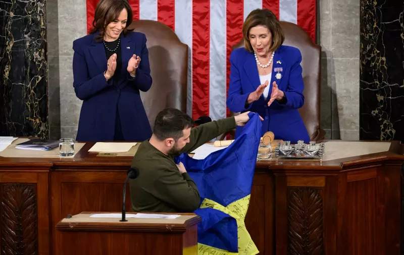 Ukraine's President Volodymyr Zelensky gives a Ukrainian national flag to US House Speaker Nancy Pelosi (D-CA) as US Vice President Kamala Harris (L) looks on during his address the US Congress at the US Capitol in Washington, DC on December 21, 2022. - Zelensky is in Washington to meet with US President Joe Biden and address Congress -- his first trip abroad since Russia invaded in February. (Photo by Mandel NGAN / AFP)