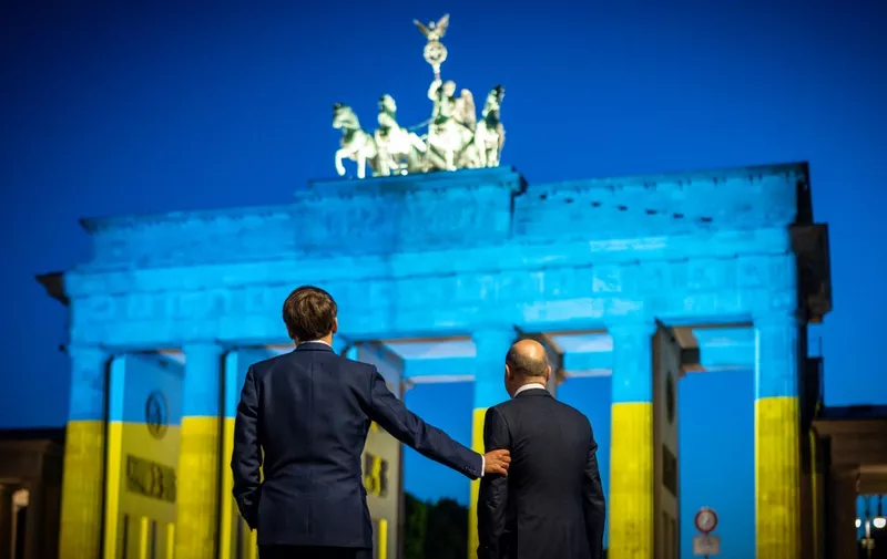 09 May 2022, Berlin: German Chancellor Olaf Scholz (r, SPD) and French President Emmanuel Macron stand in front of the Brandenburg Gate after a meeting. To mark Europe Day, the Brandenburg Gate is illuminated in Ukraine's national colors. Photo: Michael Kappeler/dpa (Photo by MICHAEL KAPPELER / DPA / dpa Picture-Alliance via AFP)