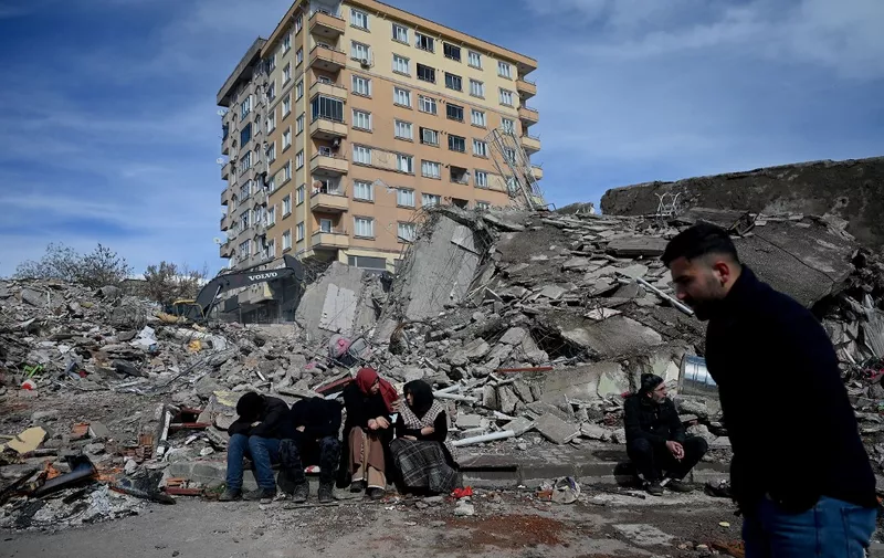 Families wait through the rubble of buildings in kahramanmaras, the quake's epicentre, after a 7.8-magnitude earthquake struck the country's southeast on February 7, 2023. - The combined death toll has risen to above 5,000 for Turkey and Syria after the region's strongest quake in nearly a century. (Photo by OZAN KOSE / AFP)