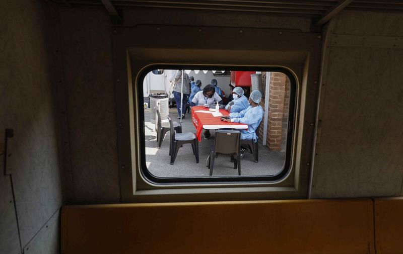 Healthcare workers wait to register people for their vaccines outside the Transvaco Covid-19 vaccine train stationed at the Springs Train Station outside of Johannesburg, on August 25, 2021. - Transvaco's role is purely to administer Covid-19 vaccines to communities which have limited healthcare resources. (Photo by Phill Magakoe / AFP)