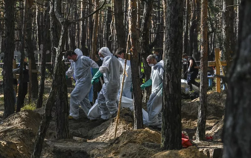 EDITORS NOTE: Graphic content / Forensic technicians carry a bodybag at the site of a mass grave in a forest on the outskirts of Izyum, eastern Ukraine on September 18, 2022. - Ukrainian authorities discovered around 450 graves outside the formerly Russian-occupied city of Izyum with some of the exhumed bodies showing signs of torture. (Photo by Juan BARRETO / AFP)