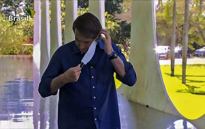 Screen grab of TV Brasil showing Brazilian President Jair Bolsonaro putting a face mask on as he prepares to speak with journalists at Planalto Palace in Brasilia on July 7, 2020. - Brazil President Jair Bolsonaro announced on Tuesday he had tested positive for the coronavirus but said he was feeling "perfectly well" and had only mild symptoms. (Photo by - / TV BRASIL / AFP)