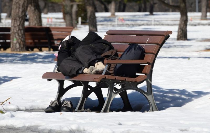 A homeless man takes a nap on a bench at a park in Tokyo on February 16, 2014 after a snow storm hit Japan. Two people were killed when a fresh snow storm hit Japan, disrupting rail and road travel, grounding more than 100 flights and adding to the piles left behind by an earlier blanketing.      AFP PHOTO/Toru YAMANAKA / AFP / TORU YAMANAKA