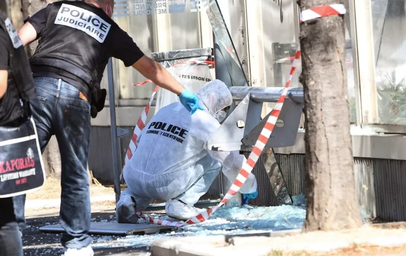 A French criminal police officer gestures as a forensic police officer searches the site following a car crash on August 21, 2017, in the southern Mediterranean city of Marseille.  
At least one person has died in Marseille after a car crashed into people waiting at two different bus stops in the southern French port city, police sources told AFP, adding that the suspected driver had been arrested afterwards. The police sources, who asked not to be identified, did not say whether the incident was being treated as a terror attack or an accident.  / AFP PHOTO / boris HORVAT