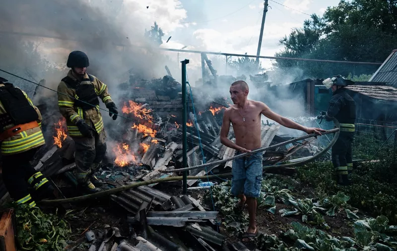 A local resident helps firefighters to put out a fire in a yard of a house in the town of Bakhmut following an airstrike on July 19, 2022, amid the Russian invasion of Ukraine. (Photo by Igor TKACHEV / AFP)
