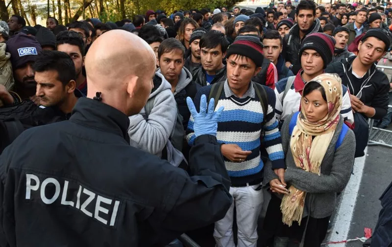 A German police officer speaks with migrants waiting to cross the Austrian-German border near the Bavarian town of Passau, southern Germany, on October 28, 2015. AFP PHTO / CHRISTOF STACHE