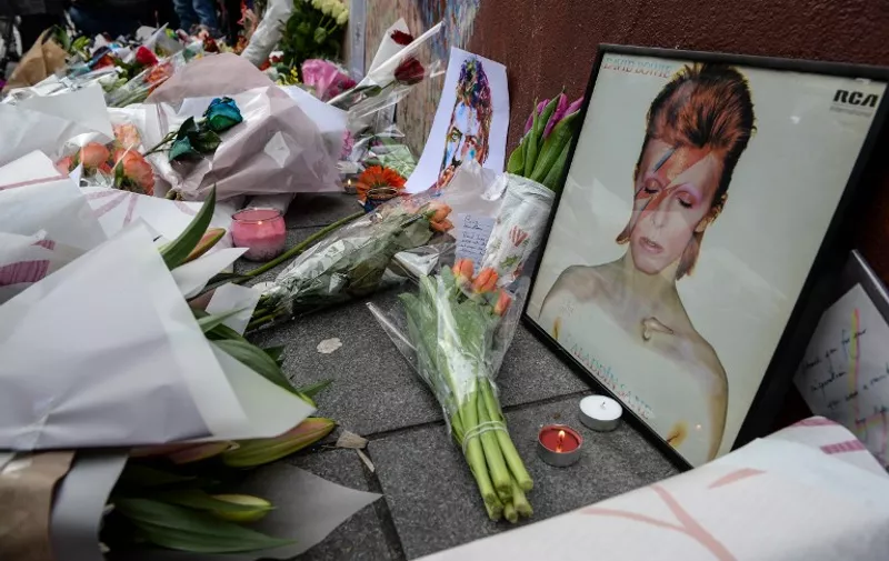 Tributes are seen beneath a mural of British singer David Bowie, following the announcement of Bowie's death, in Brixton, south London, on January 11, 2016. British music icon David Bowie died of cancer at the age of 69, drawing an outpouring of tributes for the innovative star famed for groundbreaking hits like "Ziggy Stardust" and his theatrical shape-shifting style.   AFP PHOTO / CHRIS RATCLIFFE / AFP / CHRIS RATCLIFFE