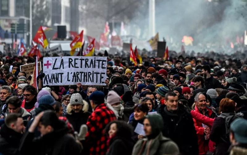 A protestor holds a placard which reads as 'retirement before arthritis' during a rally in Lyon, south-eastern France on January 19, 2023, as workers go on strike over the French President's plan to raise the legal retirement age from 62 to 64. - A day of strikes and protests kicked off in France on January 19, set to disrupt transport and schooling across the country in a trial for the government as workers oppose a deeply unpopular pensions overhaul. (Photo by OLIVIER CHASSIGNOLE / AFP)