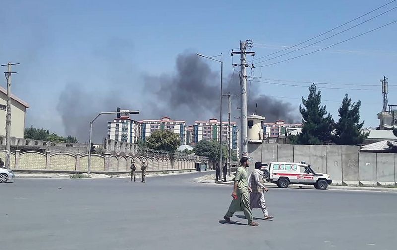 Afghan men walk on a road as smoke rises from the site of an attack in Kabul on July 1, 2019. - Dozens of people were wounded with fatalities feared as a powerful car bomb rocked Kabul early July 1, followed by gunmen battling special forces in an area housing military and government buildings, officials said. (Photo by STR / AFP)