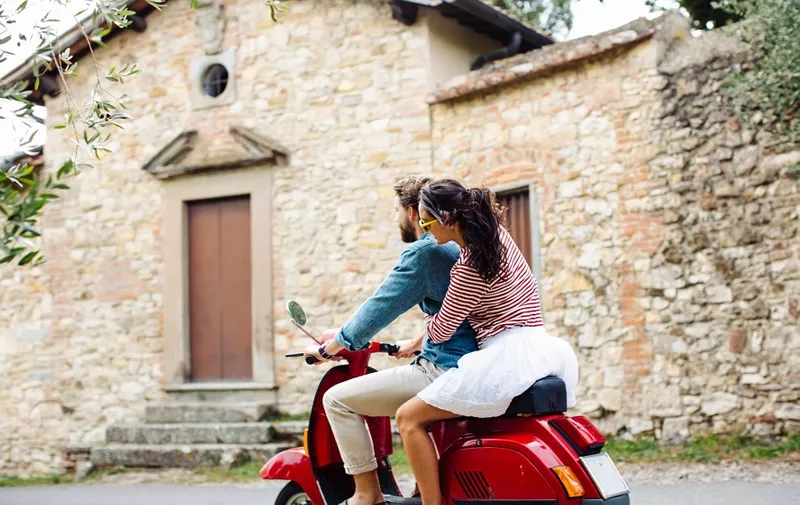 Young couple riding moped in village, Florence, Italy
