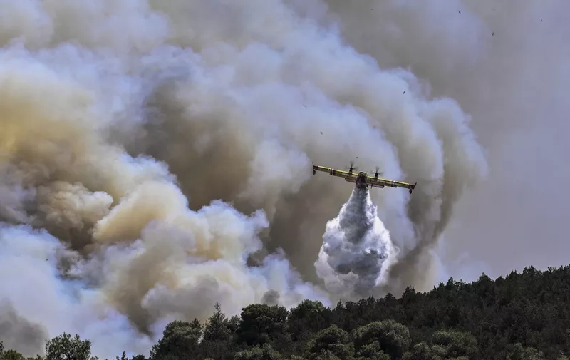 A Canadair firefighting plane sprays water during a fire in Dervenochoria, north-west of Athens, on July 19, 2023. Extreme heat was forecast across the globe on July 19, 2023, as wildfires raged and health warnings were in place in parts of Asia, Europe and North America. Firefighters battled blazes in parts of Greece and the Canary Islands, while Spain issued heat alerts and some children in Italy's Sardinia were told to stay away from sports. (Photo by Spyros BAKALIS / AFP)