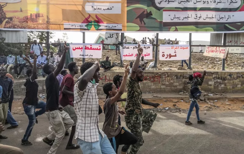 A Sudanese soldier joins anti-regime demonstrators with their protest on April 11, 2019 in the area around the army headquarters in Sudan's capital Khartoum. Arabic slogans on banners in the background praise the army and its "bold troops" and call for the fall of the regime, adding that the "voice of women is revolution". - The Sudanese army is planning to make "an important announcement", state media said today, after months of protests demanding the resignation of longtime leader President Omar al-Bashir. Thousands of Khartoum residents chanted "the regime has fallen" as they flooded the area around the military headquarters, where protesters have held an unprecedented sit-in now in its sixth day. (Photo by - / AFP)