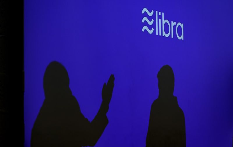 Silhouettes are seen beneath a sign of Libra, the cryptocurrency project launched by Facebook during a conference at marketing and communication school CREA in Geneva on September 26, 2019. (Photo by Fabrice COFFRINI / AFP)