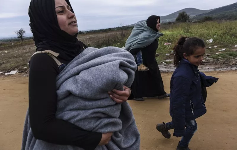 Migrants carry their children as they walk on a dirt road  after crossing the Macedonian-Serbian border near the village of Miratovac on October 21, 2015. Tens of thousands -- many fleeing violence in Syria, Africa and Afghanistan -- have been making their way from Turkey to the Balkans in recent months, hoping to reach Germany, Sweden and other EU states. AFP PHOTO / ARMEND NIMANI