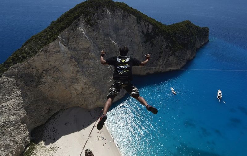 TO GO WITH AFP STORY BY FRANCOISE CHAPTAL
A jumper jumps from a platform atop the rugged rocks overlooking the azure waters of Navagio beach, one of the Greece's most renowned leisure spots on the popular tourist island of Zakynthos on June 23, 2014.  This is rope jumping -- part diving, part rock climbing, with a touch of engineering. The aim of the project is to dream jump in 80 places with most ravishing nature and architecture all over the world .They plan to stage their next leaps at a cave complex in Croatia, a French viaduct, skyscrapers in Las Vegas and Johannesburg, and the Grand Canyon. AFP PHOTO /  LOUISA GOULIAMAKI