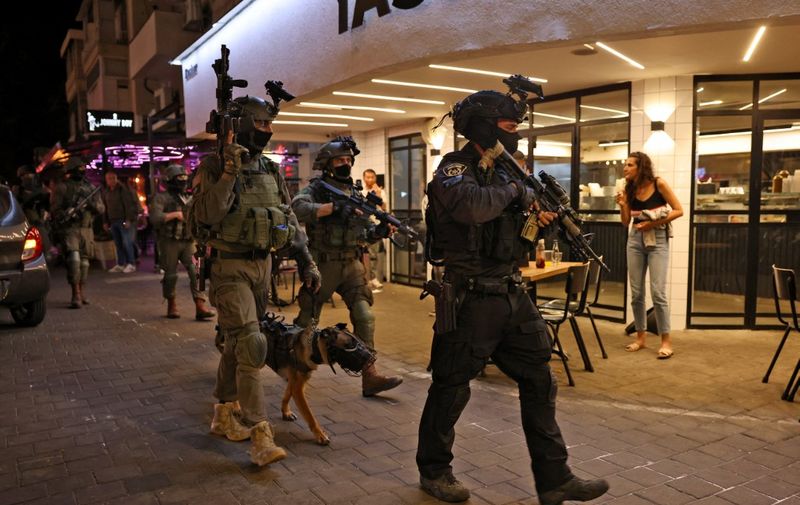 A security forces' member with a police dog walks outside a restaurant at the scene of a shooting attack in Dizengoff Street in the centre of Israel's Mediterranean coastal city of Tel Aviv on April 7, 2022. - At least two people were killed and several wounded during an attack in the Israeli city of Tel Aviv on April 7, a hospital said. It is the latest incident among a surge of violence in Israel and the West Bank since late March. (Photo by AHMAD GHARABLI / AFP)