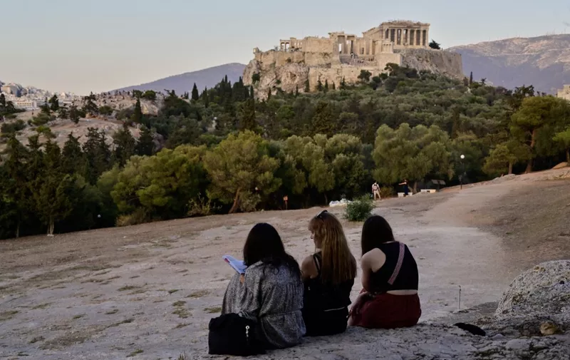 Women sit at the Filopappou hill with the Acropolis site in the background in Athens on May 25, 2023. (Photo by Louisa GOULIAMAKI / AFP)