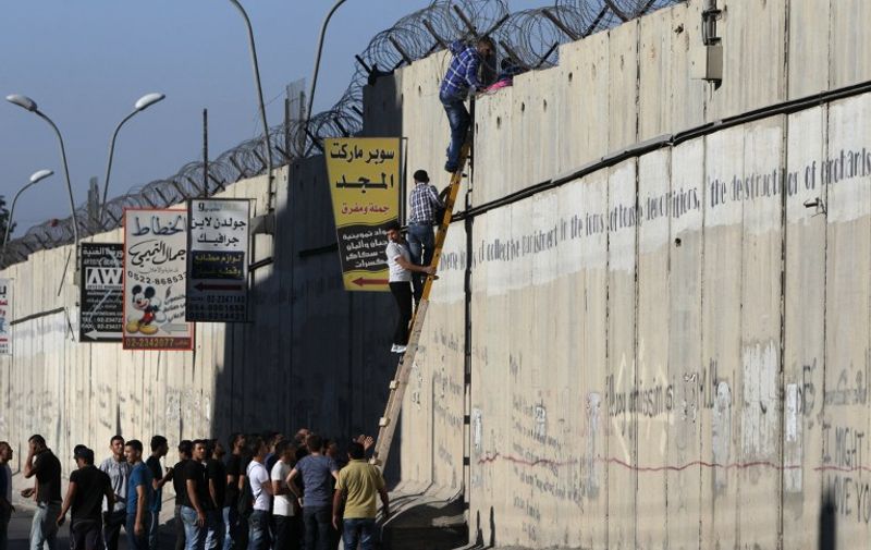 Palestinian men climb a section of Israel's separation barrier as they try to avoid crossing Israeli-controlled checkpoints to reach  the al-Aqsa mosque compound in Jerusalem's Old City,  on July 26, 2013, on the third Friday of the holy month of Ramadan. Muslims fasting in the month of Ramadan must abstain from food, drink and sex from dawn to dusk, when they break the fast with a meal known as Iftar. AFP PHOTO/