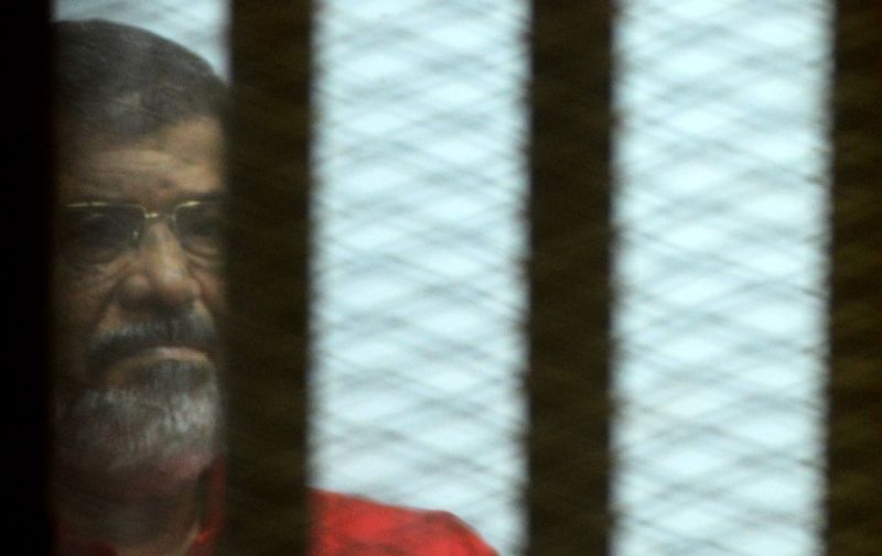 Egypt's ousted Islamist president Mohamed Morsi, wearing a red uniform, looks on from behind the defendant's bars during his trial on espionage charges at a court in Cairo on June 18, 2016.
An Egyptian court sentenced Morsi to life in prison in an espionage trial in which six co-defendants were handed death penalties.The court acquitted Morsi of charges of having supplied Qatar with classified documents but sentenced him to life for leading an unlawful organisation.
 / AFP PHOTO / MOHAMED EL-SHAHED