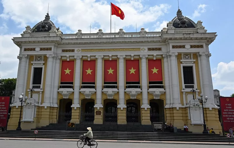 A woman rides a bicycle past the Hanoi Opera House in Hanoi on August 30, 2023. (Photo by Nhac NGUYEN / AFP)