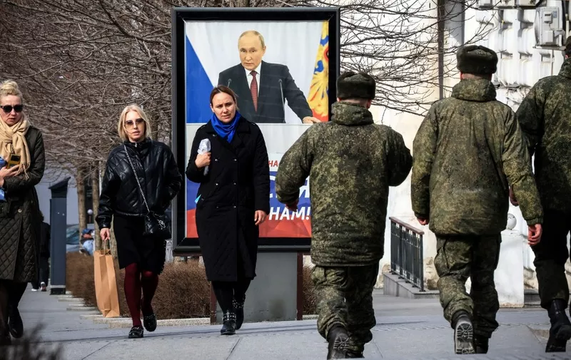 People walk in front of a poster showing Russian President Vladimir Putin and reading "The West doesn't need Russia. We need Russia!"  in Simferopol, Crimea, on March 5, 2024. (Photo by STRINGER / AFP)