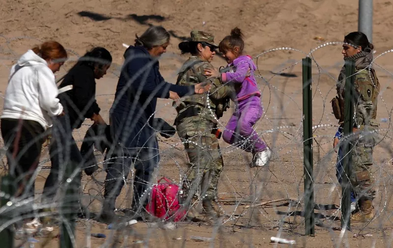 A Texas National Guard agent carries a migrant girl over a barbed fence on the banks of the Rio Grande in El Paso, state of Texas, United States, border with Ciudad Juarez, state of Chihuahua, Mexico on January 30, 2024. (Photo by HERIKA MARTINEZ / AFP)