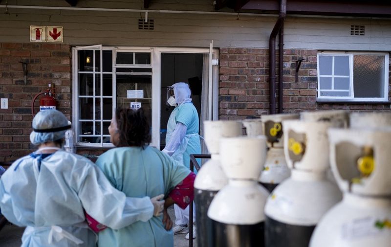 A health worker looks on as another helps a COVID-19 patient back to her room in a non-profit COVID-19 care facility in Norwood, Johannesburg on July 12, 2021. (Photo by Emmanuel Croset / AFP)