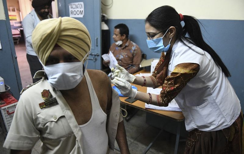 A medical worker inoculates a policeman with a dose of the Covishield, ChAdOx1 nCoV-19 coronavirus vaccine, at a civil hospital in Ajnala village, about 28 km from Amritsar on April 1, 2021, as India expanded its coronavirus vaccination drive to the 45-60 age group. (Photo by NARINDER NANU / AFP)