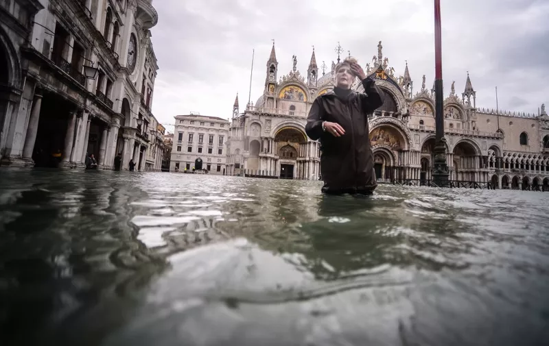 A general view shows a woman walking across the flooded St. Mark's Square, by St. Mark's Basilica (Rear) on November 15, 2019 in Venice, two days after the city suffered its highest tide in 50 years. - Flood-hit Venice was bracing for another exceptional high tide on November 15, as Italy declared a state of emergency for the UNESCO city where perilous deluges have caused millions of euros worth of damage. (Photo by Filippo MONTEFORTE / AFP)