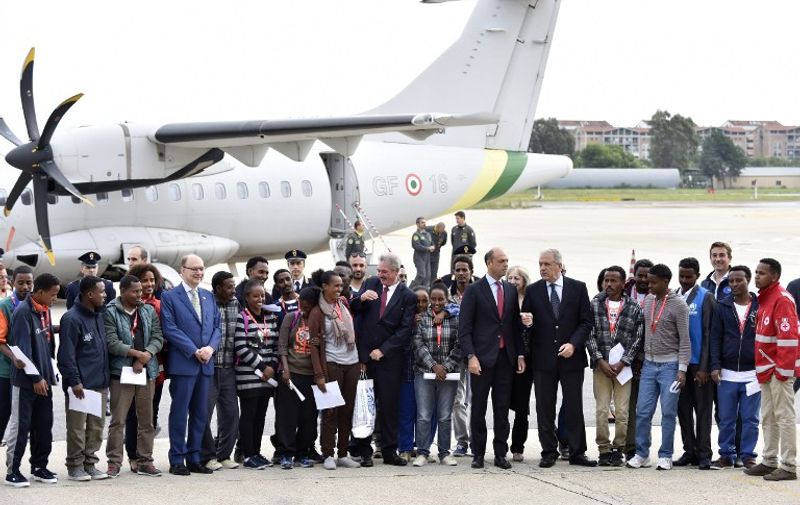 Italian Interior Minister Angelino Alfano (7thR), EU Commissioner Dimitris Avramopoulos (6thR) and Luxembourg Minister of Foreign and European Affairs Jean Asselborn (C) pose with a group of Eritrean refugees before the take off of their plane to Sweden as part of a new programme of the European Union to relocate refugees on October 9, 2015 at the Ciampino airport of Rome. A small group of Eritreans left Italy for Sweden, the first contingent of asylum-seekers to be relocated under a European Union scheme to ease the burden of the migration crisis on frontline countries. Grinning shyly before the media, 19 young Eritreans shook hands with EU migration commissioner Dimitris Avramopoulos and waved as they boarded a financial police plane at Rome's Ciampino airport.   AFP PHOTO / ANDREAS SOLARO