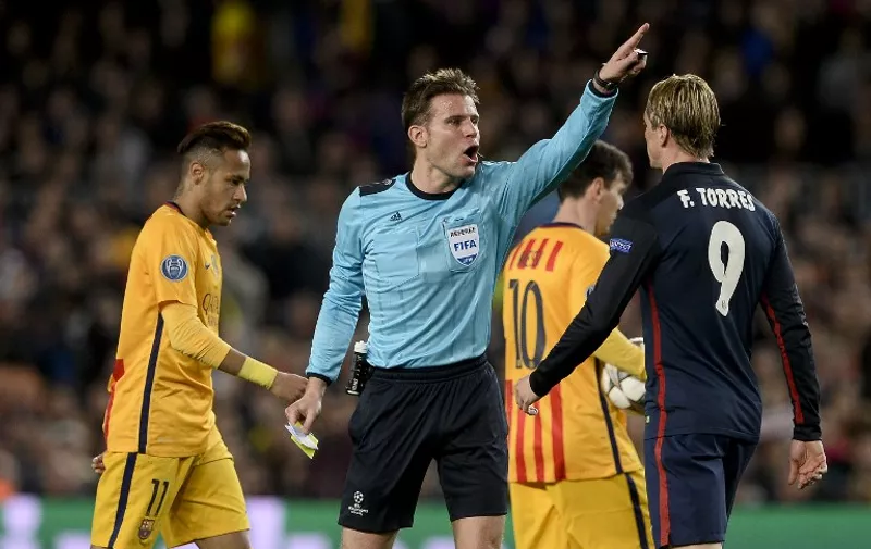 German referee Felix Brych (C) gestures after showing a yellow card to Atletico Madrid's forward Fernando Torres (R) during the UEFA Champions League quarter finals first leg football match FC Barcelona vs Atletico de Madrid at the Camp Nou stadium in Barcelona on April 5, 2016. / AFP / JOSEP LAGO
