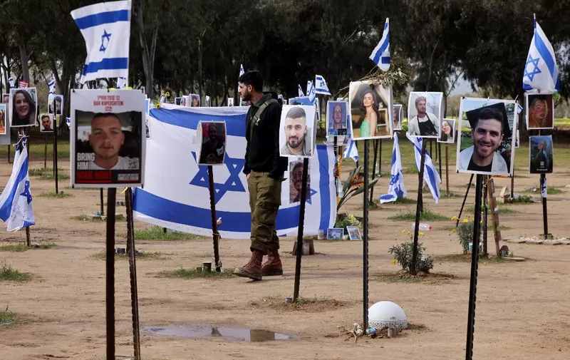 An Israeli soldier walks past national flags and portraits of Israeli people taken captive or killed by Hamas militants during the October 7 attacks, during a visit at the site where the Supernova music festival took place near Kibbutz Reim in southern Israel, on January 14, 2024, after 100 days of war between Israel and the militant Hamas group in Gaza. (Photo by Menahem KAHANA / AFP)