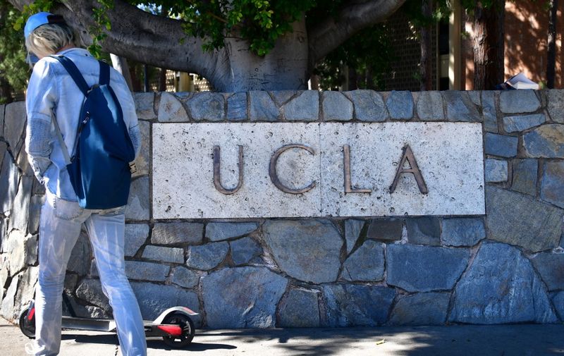 A man with a backpack walks past a sign at the University of California Los Angeles (UCLA) in Los Angeles, California on March 13, 2019. - Thirteen people, including Hollywood Stars and people with ties to UCLA and the University of Southern California (USC) were among more than 50 people arrested on March 12 in a college entrance exam scheme involving wealthy parents and elite universities. "Desperate Housewives" star Felicity Huffman and fellow Hollywood actress Lori Loughlin were among dozens indicted on March 12, 2019 in a multi-million dollar scam to help children of the American elite cheat their way into top universities, including USC. (Photo by Frederic J. BROWN / AFP)