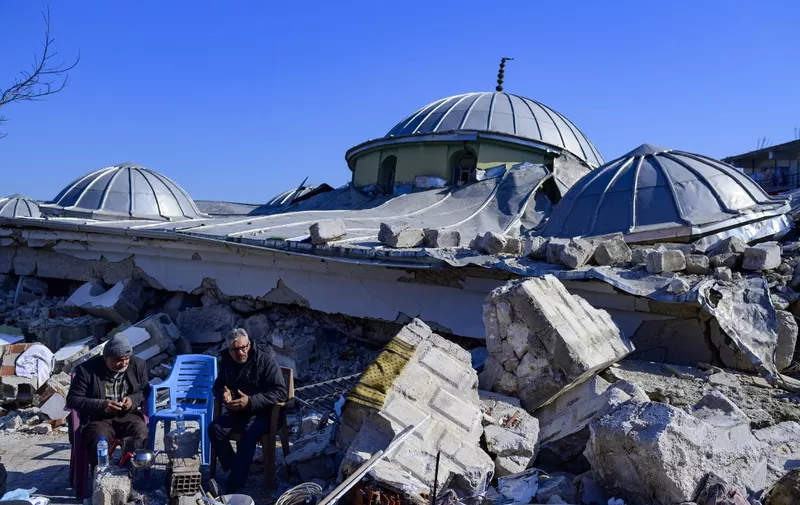 Local residents sit next to the rubble of a destroyed mosque in Hatay, on February 10, 2023, after the 7.8 magnitude earthquake that killed over 11.200 people. - Searchers were still pulling survivors on February 8 from the rubble of the earthquake that killed over 11,200 people in Turkey and Syria, even as the window for rescues narrowed. For two days and nights since the 7.8 magnitude quake, thousands of searchers have worked in freezing temperatures to find those still alive under flattened buildings on either side of the border. (Photo by Yasin AKGUL / AFP)